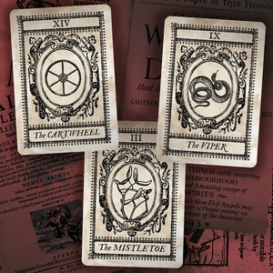 May include: Four vintage tarot cards with black and white illustrations. The cards are titled "The Cartwheel", "The Viper", "The Mistletoe", and "IX". The cards are on a red and white background.