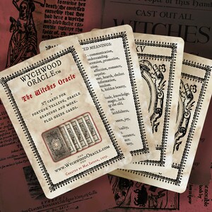 May include: A close-up of a set of tarot cards with a vintage aesthetic. The cards feature a black and white design with a decorative border. The cards are titled "The Witches Oracle" and feature the text "27 cards for fortune telling, oracle readings and more. Plus guide cards." The cards are laid out on a table with a red and white background.