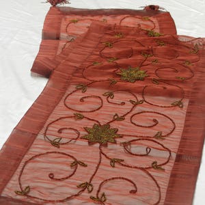 May include: A red sheer table runner with a gold beaded floral design. The runner has a scalloped edge and is perfect for adding a touch of elegance to any table.