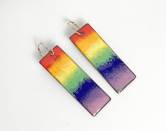 May include: A pair of rainbow enamel earrings with gold hooks. The earrings are rectangular and have a gradient of colors from red to purple.