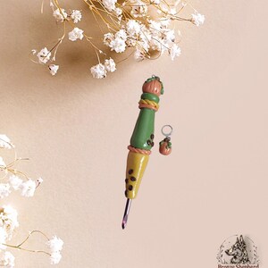 May include: A handmade crochet hook with a pumpkin-themed design. The hook features a green and yellow handle with brown coffee bean accents and a pumpkin-shaped top. A matching pumpkin charm earring is also included.