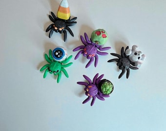May include: A collection of handmade Halloween-themed spider figurines. The spiders are in various colors, including black, green, and purple, and are decorated with candy corn, eyeballs, and other spooky elements. Perfect for Halloween decorations.