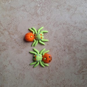 May include: Two green and orange Halloween spider ornaments with pumpkin faces.