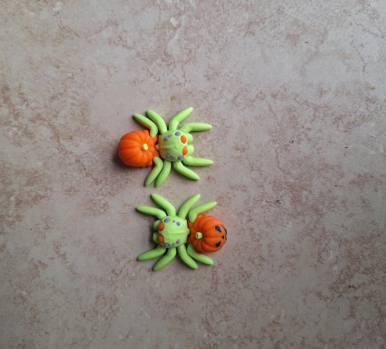 May include: Two green and orange Halloween spider ornaments with pumpkin faces.