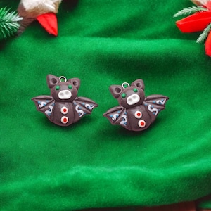 May include: Two brown bat ornaments with white and blue details, green eyes, and red accents. The bats are on a green velvet surface.