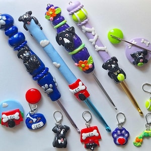 Op de afbeelding: Een set van 10 haaknaalden met hondenthema toppers. De toppers zijn gemaakt van polymer clay en hebben zwarte honden, botten, tennisballen en voetafdrukken. De haaknaalden zijn in verschillende kleuren, waaronder blauw, paars en goud. De haaknaalden zijn gelabeld "Leo" en hebben een hondenhok ontwerp.