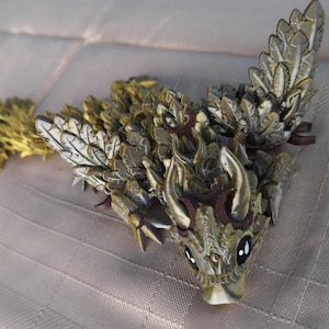Puede incluir: Una figurita de dragón dorada y marrón con detalles intrincados y una superficie texturizada. El dragón tiene alas grandes y una cola larga.