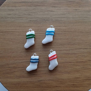 Puede incluir: Cuatro adornos de calcetines de Navidad de cerámica blanca con rayas de diferentes colores. Los calcetines tienen un lazo plateado para colgar. Las rayas son rojas, azules, verdes y azul verdoso.