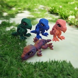 Puede incluir: Cuatro pequeñas figuritas de dinosaurio articuladas en diferentes colores: verde, azul, rosa y morado. Las figuritas están posadas en una variedad de posiciones dinámicas.