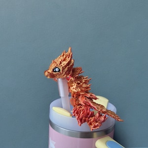 May include: A red and orange dragon-shaped bottle stopper with black eyes sits on top of a pink and yellow water bottle.