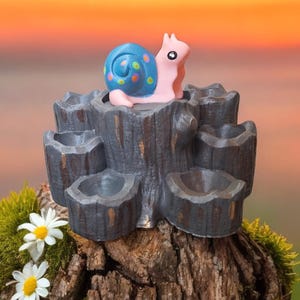 May include: A small, gray, wooden tree stump with six holes around the top. A pink and blue snail with colorful dots is sitting on top of the stump.