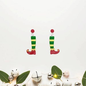 May include: A pair of elf leg dangle earrings with green and yellow striped legs and red shoes. The earrings have red tops.
