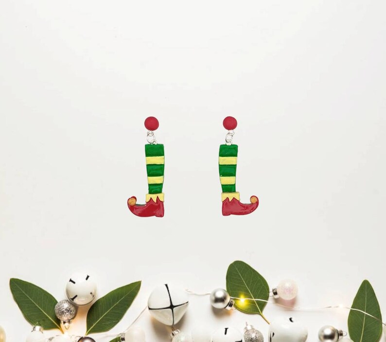May include: A pair of elf leg dangle earrings with green and yellow striped legs and red shoes. The earrings have red tops.