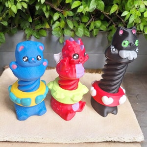 May include: Three colorful spring toys with animal faces. A blue bear, a red dragon, and a black cat. Each toy has a spring body and a colorful base.