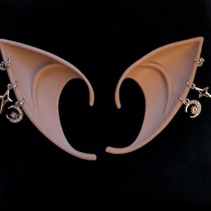 May include: A pair of elf ears with three dangling charms on each ear. The charms are a crescent moon with a star, a star, and a small bead.