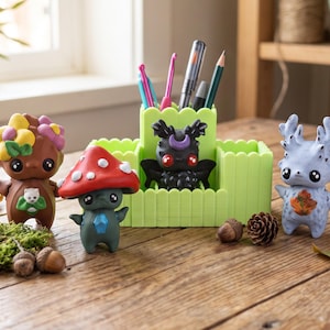 May include: A light green picket fence-style desk organizer holding pens and crochet hooks, surrounded by three small figurines: a brown creature with yellow flowers, a dark gray mushroom-capped figure, and a light blue antlered creature.