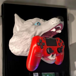 Może przedstawiać: Biała rzeźba głowy wilka z otwartymi ustami trzymająca czerwony kontroler PlayStation 4.
