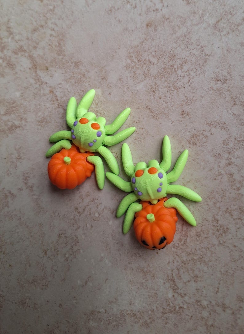 May include: Two green and purple spiders with orange pumpkins. The pumpkins have jack-o'-lantern faces.