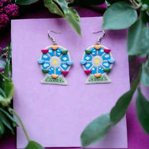 May include: A pair of earrings featuring a blue Ferris wheel design with colorful accents. The earrings are made of polymer clay and have a gold hook.