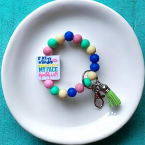 May include: A colorful silicone beaded keychain with a charm that says "If my mouth doesn't say it my face definitely will!" The charm has a pink lip design. The keychain has a green tassel.