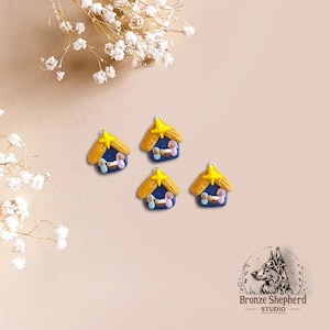 May include: Four small blue and gold Christmas ornaments shaped like a stable with a yellow star on top. The ornaments feature a yellow star, a blue stable, and three figures inside the stable.