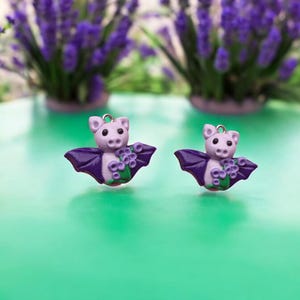 May include: Two purple and pink bat charms with lavender flowers. The charms are made of polymer clay and have a shiny finish.