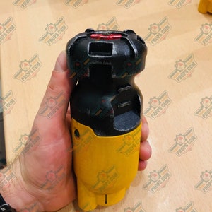 May include: A yellow and black handheld device with a red button on top. The device has a textured surface and a black handle.