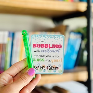 May include: A blue and white card with the text "I'm BUBBLING with excitement to have you in my CLASS this year! Mrs. Teacher" and a green bubble wand.