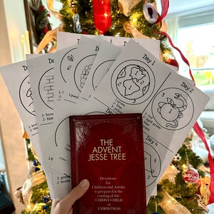 May include: A red book titled "The Advent Jesse Tree" with the text "Devotions for Children and Adults to prepare for the coming of the Christ Child at Christmas". The book is being held in front of a Christmas tree with several white sheets of paper with black and white drawings of a tree, a star, and a globe.