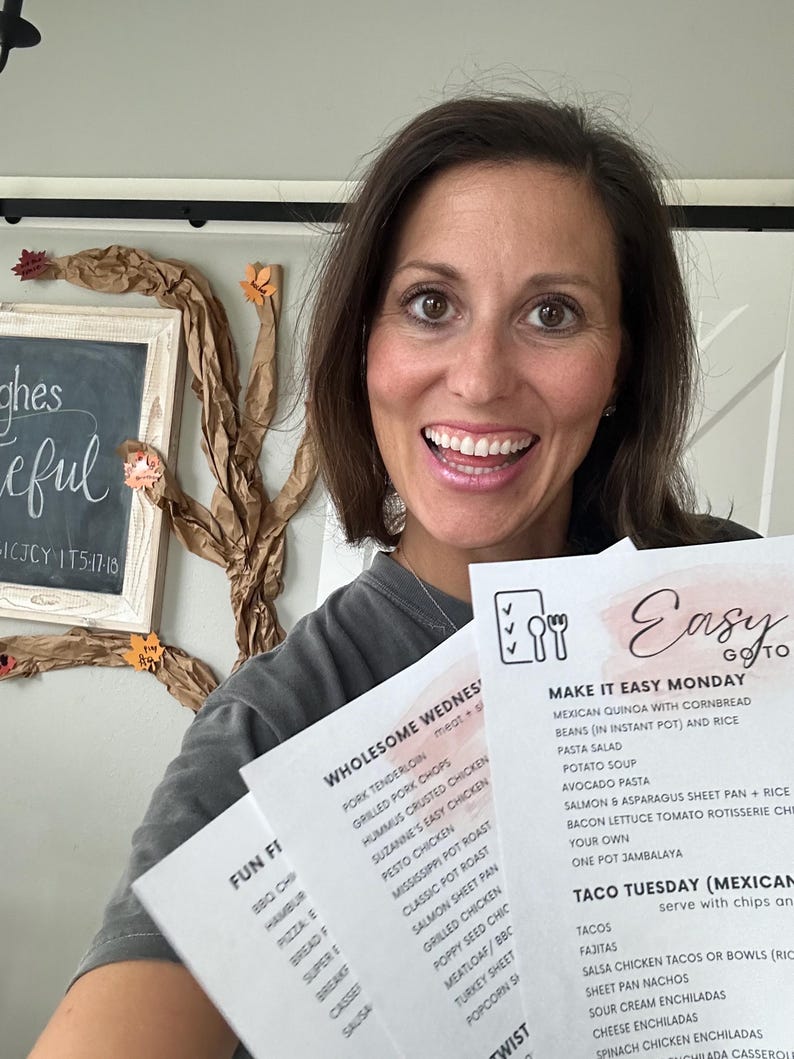 May include: A woman smiling and holding three printed menu sheets. The menus feature meal plans for the week, including options like tacos, pasta salad, and chicken dishes. The background includes a chalkboard with the words "ghes" and "eful".