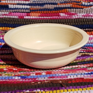 May include: A large, cream-colored ceramic bowl with a smooth, rounded rim. The bowl is sitting on a colorful woven rug.