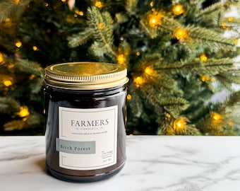 May include: A brown glass candle jar with a gold lid. The label reads "Farmers Candle Co." and "Birch Forest". The candle is 7 oz and hand-poured.