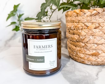 May include: A brown glass candle jar with a gold lid. The label reads "Farmers Candle Co. Sustainable Tallow & Beeswax Candle Oakmoss + Amber 7oz (198g) Hand Poured 50 hrs"