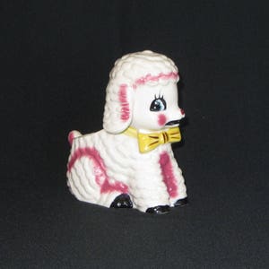 May include: A white ceramic lamb planter with pink and white fur details. The lamb has a yellow bow tie and black eyes.
