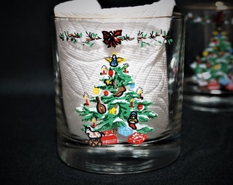 May include: Two clear glass tumblers with a Christmas tree design. The tumblers have a white paper napkin inside with a red bow. The Christmas tree is decorated with ornaments, lights, and a star on top.