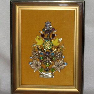 May include: A framed artwork featuring a yellow, green, and blue jeweled tree design on a mustard yellow background.