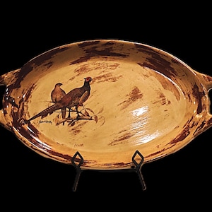 May include: A ceramic oval serving tray with brown and tan glaze and a painted image of two pheasants on a branch. The tray has two handles on the sides.