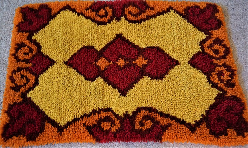 May include: A vintage rug with a geometric pattern in shades of orange, yellow, and red. The rug has a fluffy texture and a unique design.
