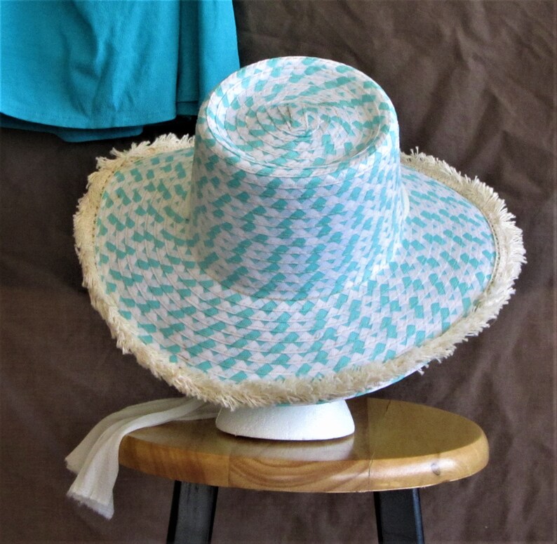 May include: A white and turquoise straw hat with a frayed brim. The hat is sitting on a wooden stool.