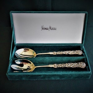 Puede incluir: Un juego de cubiertos para ensalada de plata en una caja de terciopelo verde con el logotipo de Neiman Marcus. Los cubiertos tienen un diseño ornamentado.