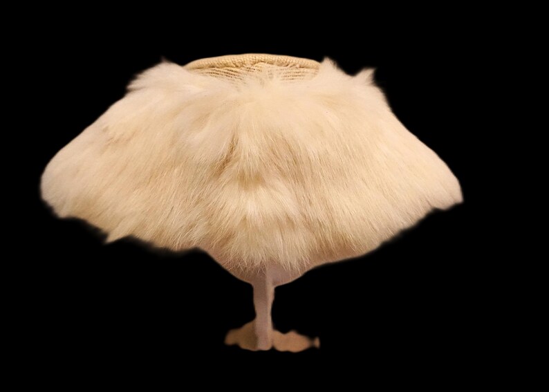 May include: A vintage-style hat with a cream-colored fur brim and a woven top. The hat is displayed on a stand against a black background, showcasing its unique design and texture. This accessory is perfect for costume parties or vintage fashion.