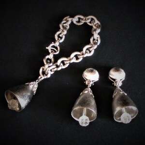 May include: A silver chain bracelet with a bell charm and a pair of silver bell earrings with clear crystal accents.