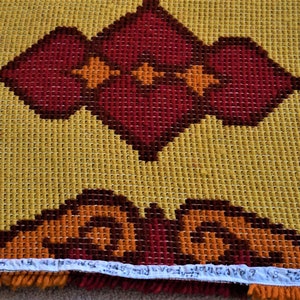 May include: A close-up of a yellow, orange, and red rug with a geometric pattern. The rug has a fringe border.