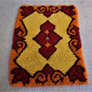 May include: A small, rectangular rug with a geometric pattern in shades of orange, yellow, and red. The rug has a thick, fluffy texture.