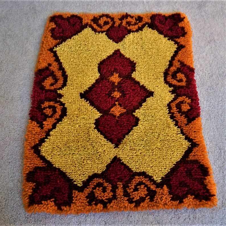 May include: A small, rectangular rug with a geometric pattern in shades of orange, yellow, and red. The rug has a thick, fluffy texture.