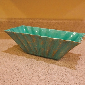May include: A turquoise ceramic bowl with a fluted design and gold accents. The bowl is rectangular in shape and has a wide, shallow opening.
