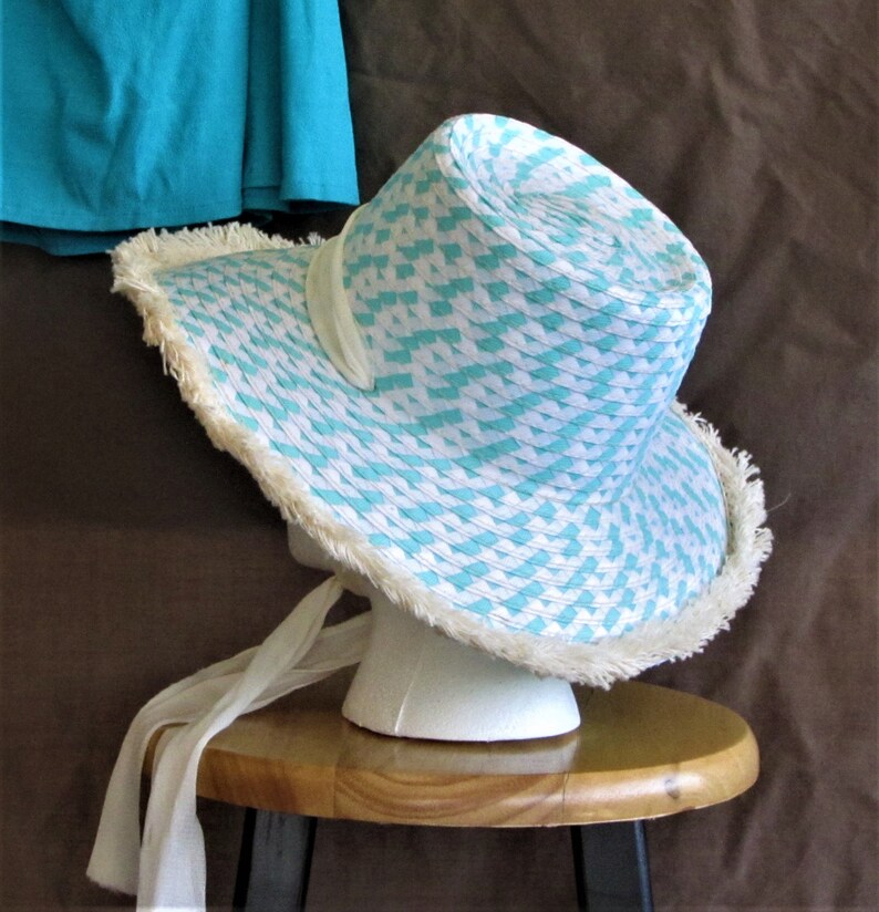 May include: A white and turquoise straw sun hat with a white trim and a white ribbon. The hat is sitting on a wooden stool.