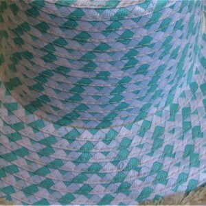 May include: A wide-brimmed straw hat with a white and turquoise woven pattern and a frayed edge.