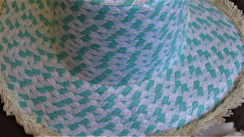 May include: A wide-brimmed straw hat with a white and turquoise woven pattern and a frayed edge.