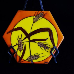 May include: A hexagonal ceramic tile featuring a yellow sun and brown wheat stalks against an orange background.